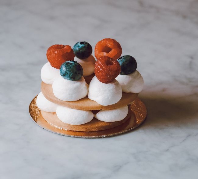 Mini crostatina da dessert con crema bianca, frutti di bosco arancioni e mirtilli su una base di marmo.