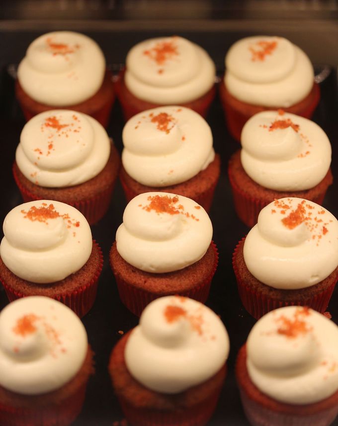 Cupcake assortiti al velluto rosso con glassa bianca e zuccherini arancioni, disposti in file su un vassoio.