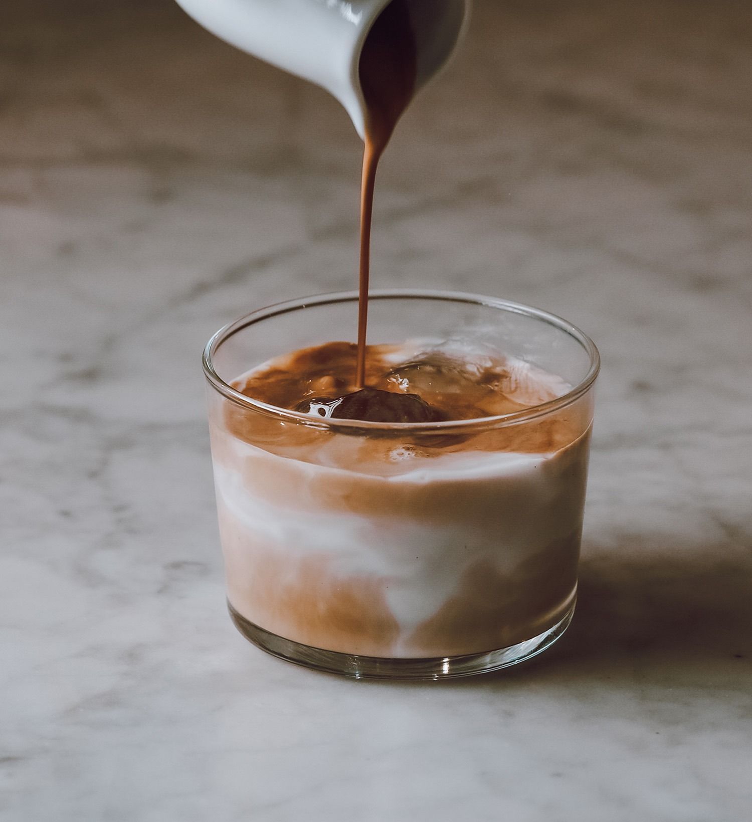 Il caffè viene versato in un bicchiere trasparente con ghiaccio su una superficie di marmo.