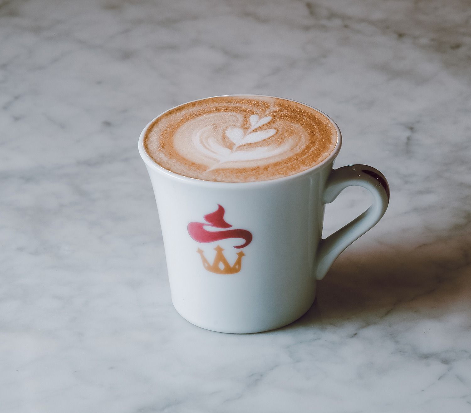 Tazza bianca con decorazione a latte art su un piano di lavoro in marmo.