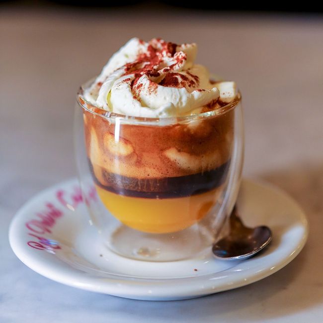 Dessert al caffè a strati in un bicchiere con panna montata e sciroppo di cioccolato su un piattino, con un cucchiaio