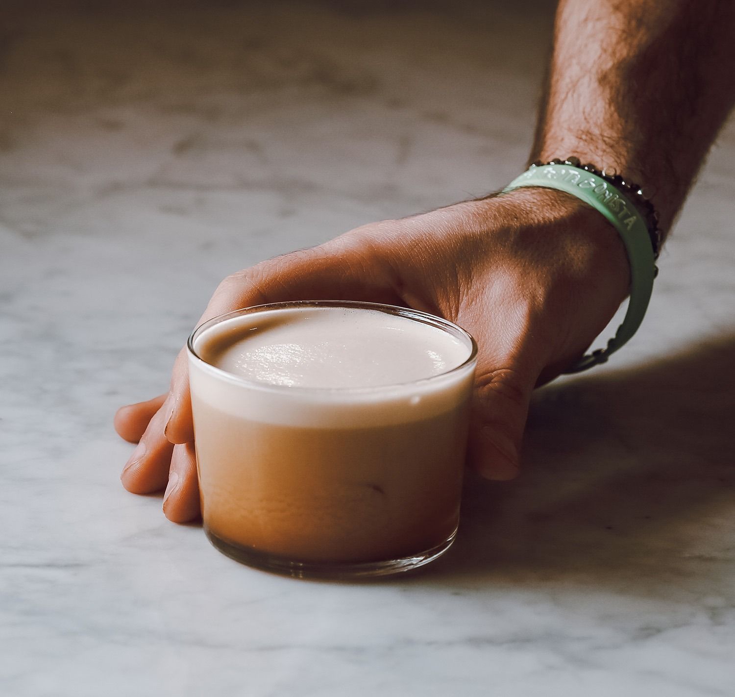 Una mano che regge una tazza di caffè schiumoso su una superficie di marmo.