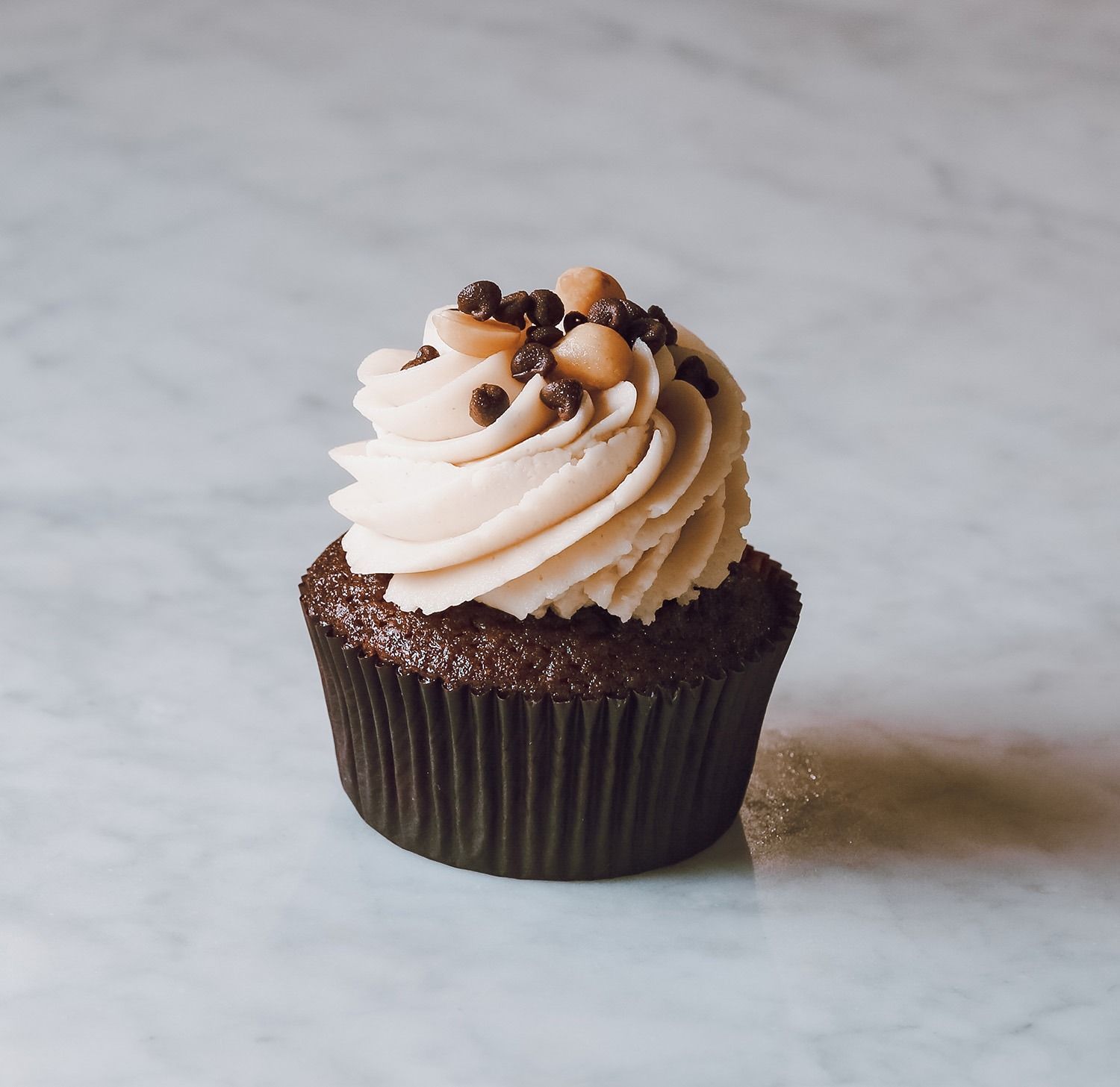 Cupcake al cioccolato con glassa leggera a spirale e granella di cioccolato su una superficie marmorizzata.