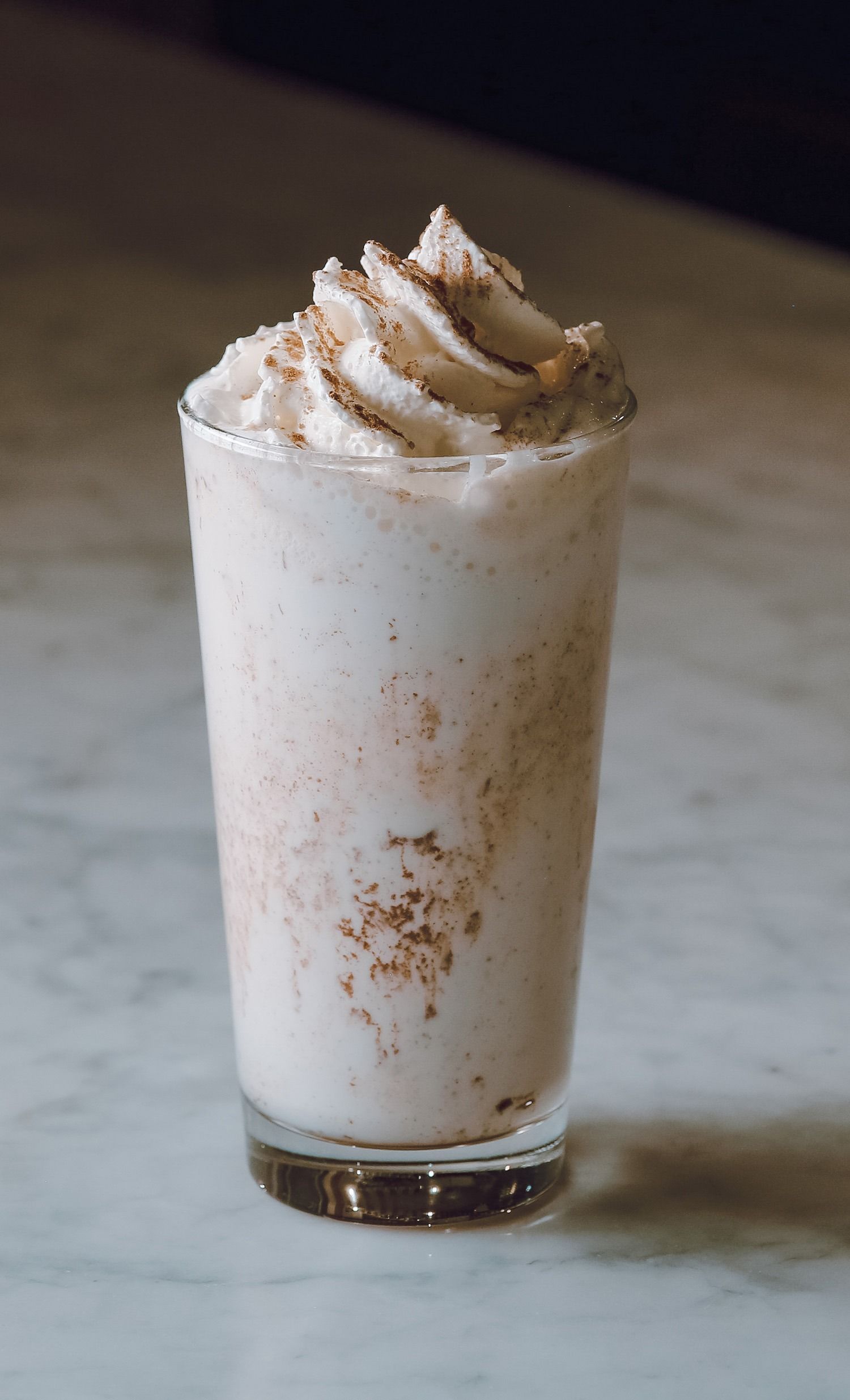 Un bicchiere alto di frappè bianco guarnito con panna montata e cannella su un tavolo