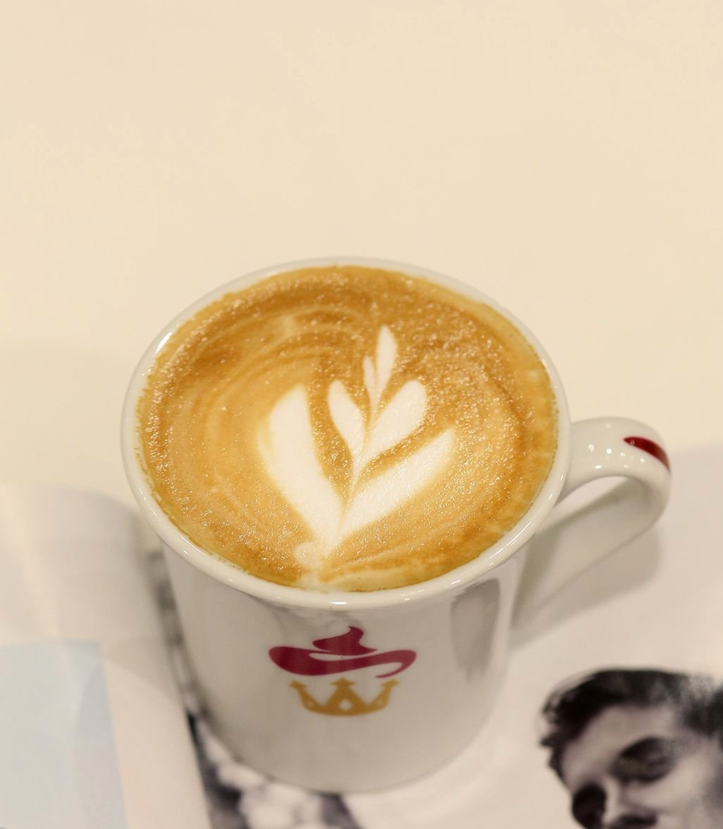 Latte con decorazione a foglia in una tazza bianca su piattino