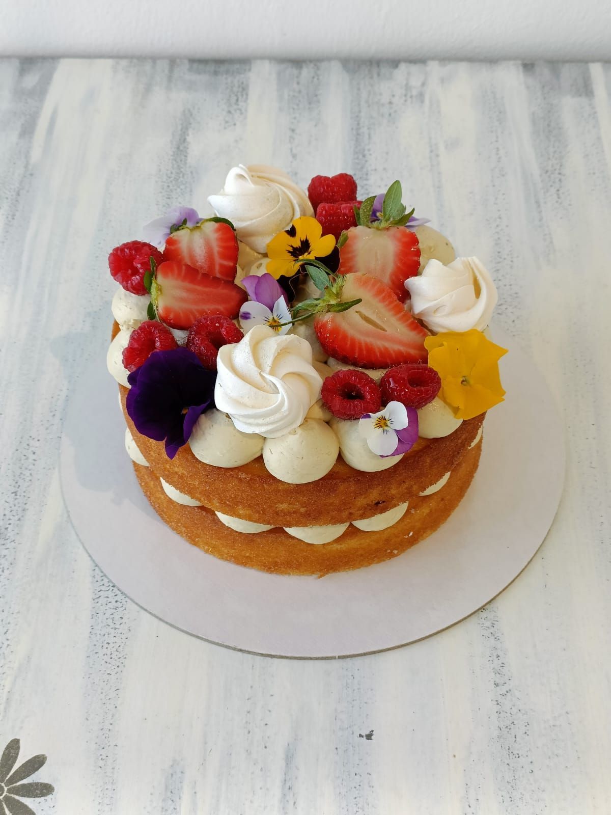 Torta a strati con frutta e panna montata, servita su un vassoio bianco.