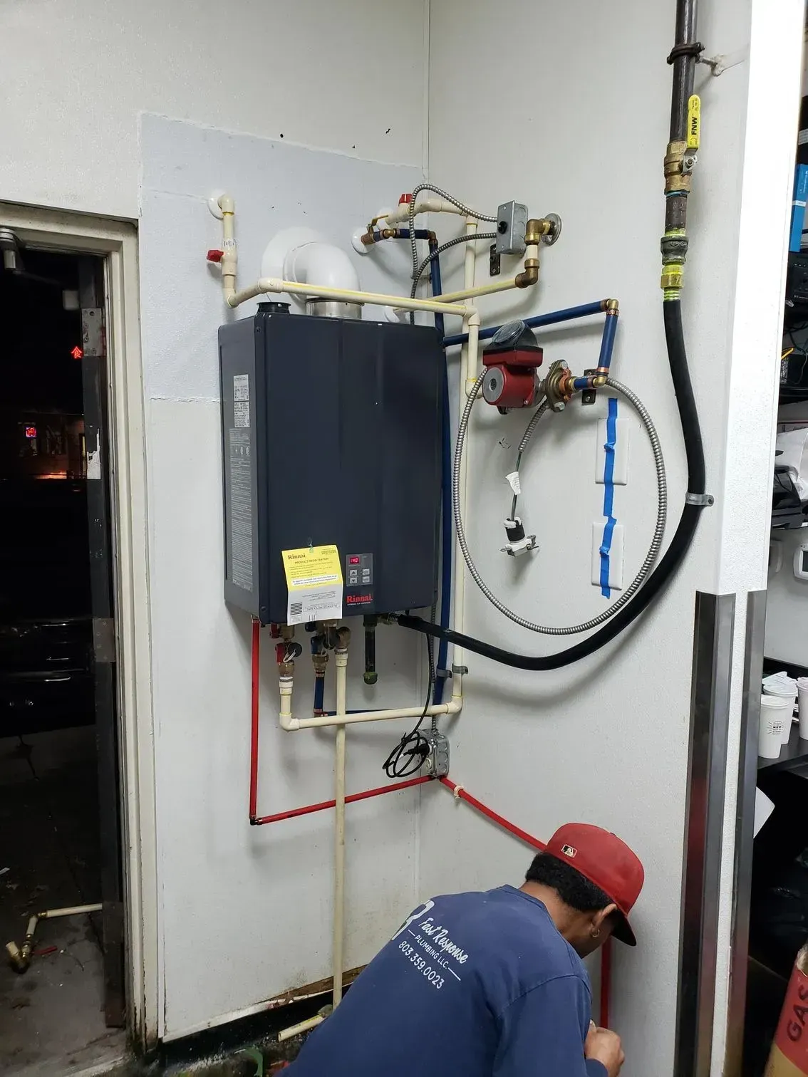Technician crouches by a wall-mounted boiler and pipes in a utility room.
