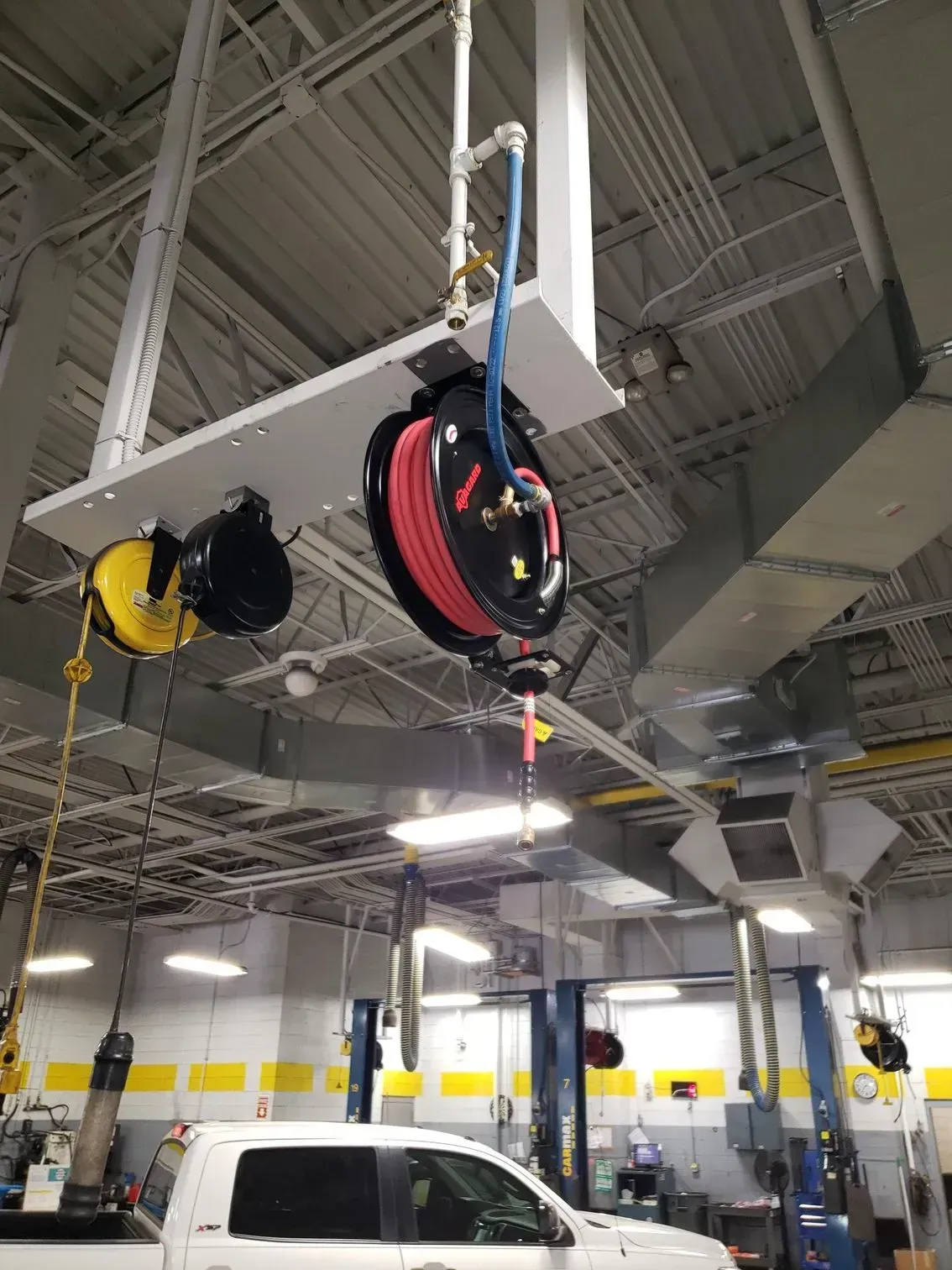 Auto shop ceiling with a hanging red hose reel and yellow reel above a white van