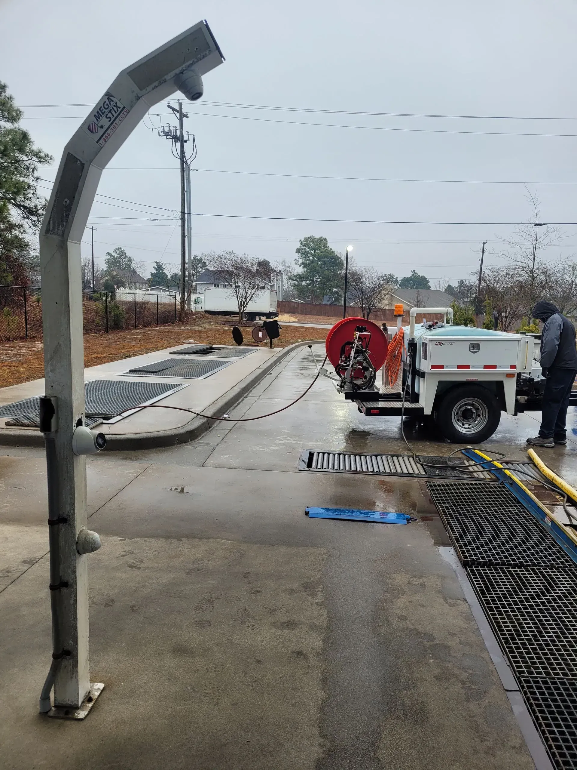 Roadwork scene with utility truck, workers, and a large concrete pipe trench on a wet street.