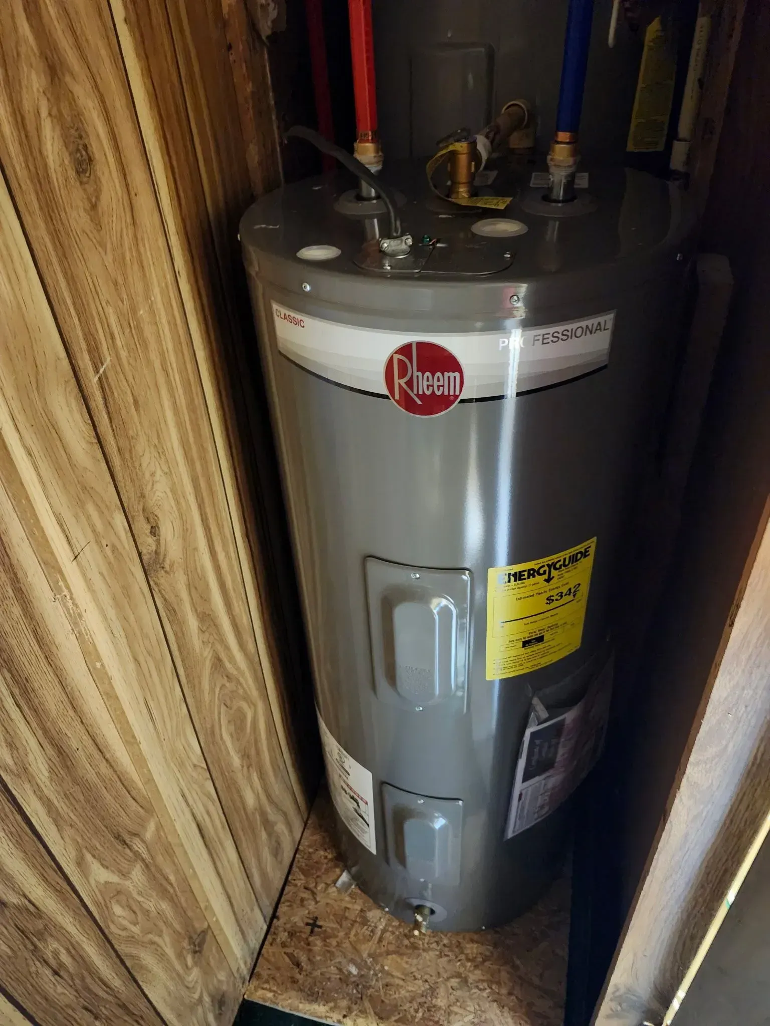 Water heater in a narrow closet, with pipes and a temperature warning label.