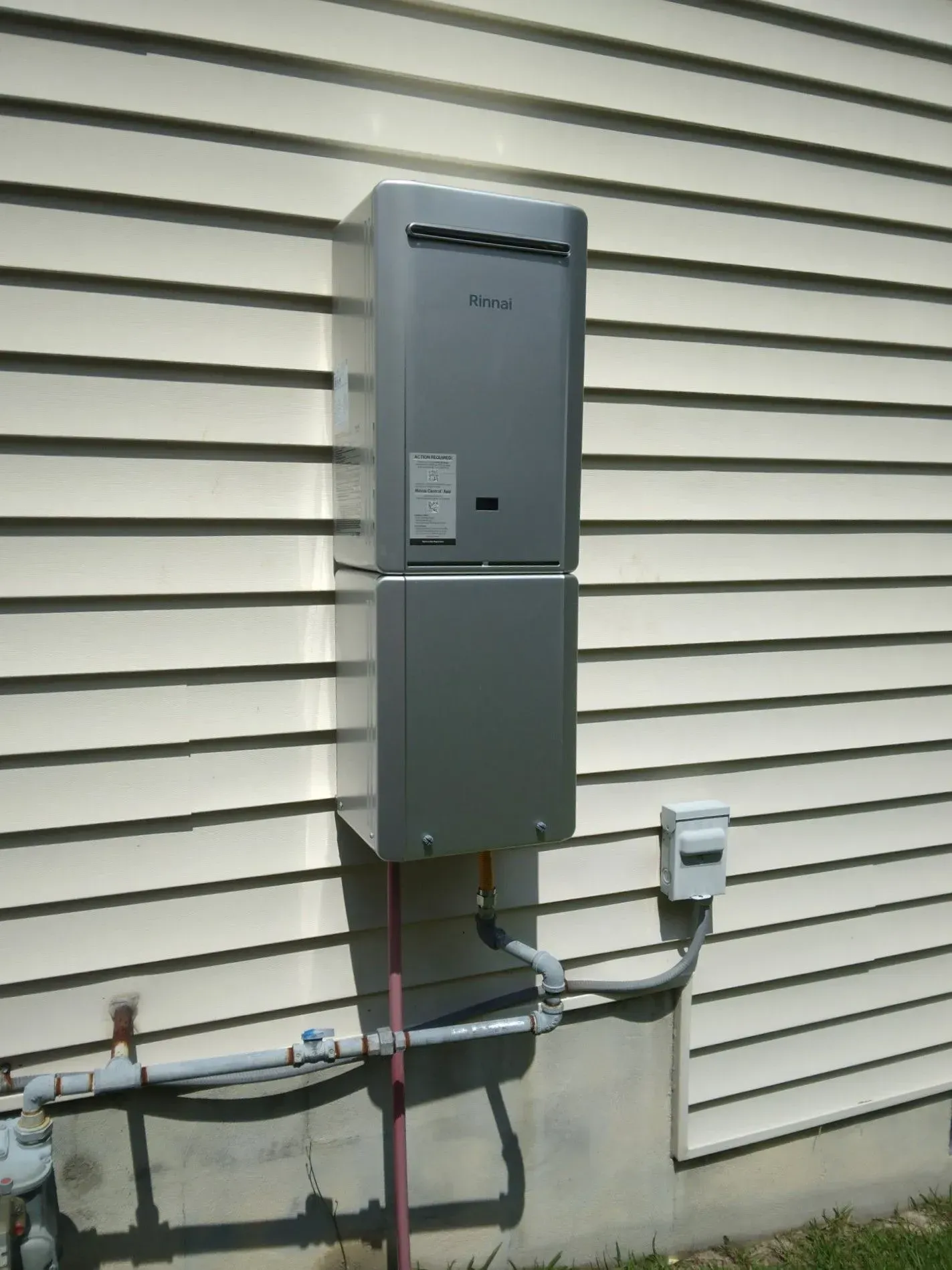 Wall-mounted gray utility meter box on a house exterior with pipes and cables.