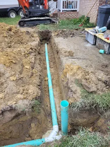 Trenched blue PVC pipes in a dug-up yard, with an excavator in the background.