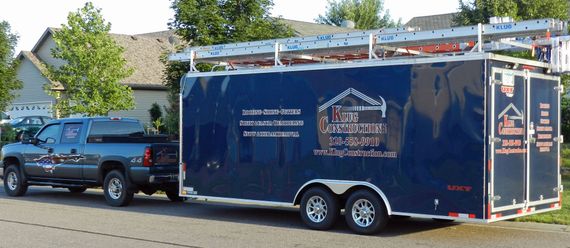 Blue enclosed trailer with white logo parked beside a black pickup truck on a suburban street