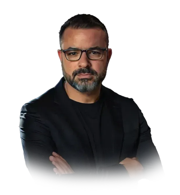 Um homem de óculos e barba está de pé com os braços cruzados.