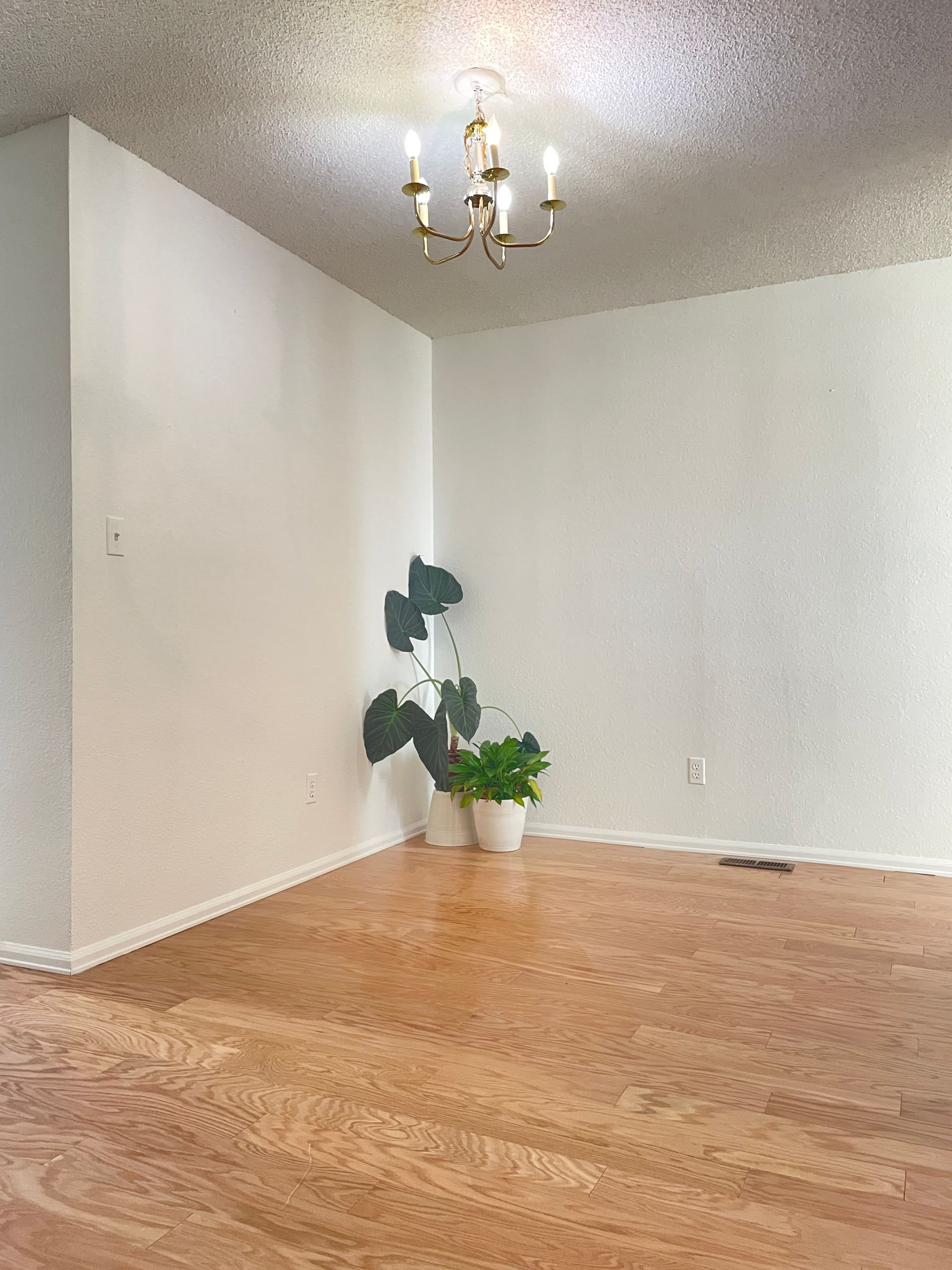 An empty living room with hardwood floors and a chandelier hanging from the ceiling.