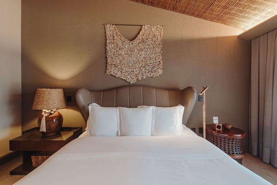 Um quarto com uma cama de casal queen-size, roupa de cama branca, cabeceira estofada marrom, duas mesas de cabeceira, luminárias e decoração de parede.