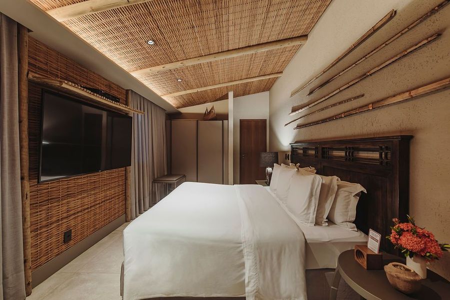 Um quarto moderno em tons quentes com uma cama branca, teto de madeira trançada, paredes texturizadas e uma grande televisão fixada na parede.