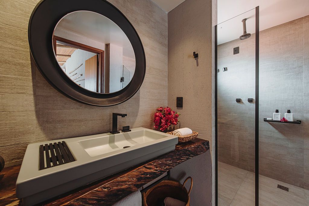 Modern bathroom with a round mirror over a rectangular sink, a marble-topped vanity, and a glass-enclosed shower.