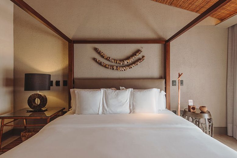 A canopy bed with crisp white linens, flanked by wooden nightstands, featuring wall-mounted driftwood decor in a bedroom.
