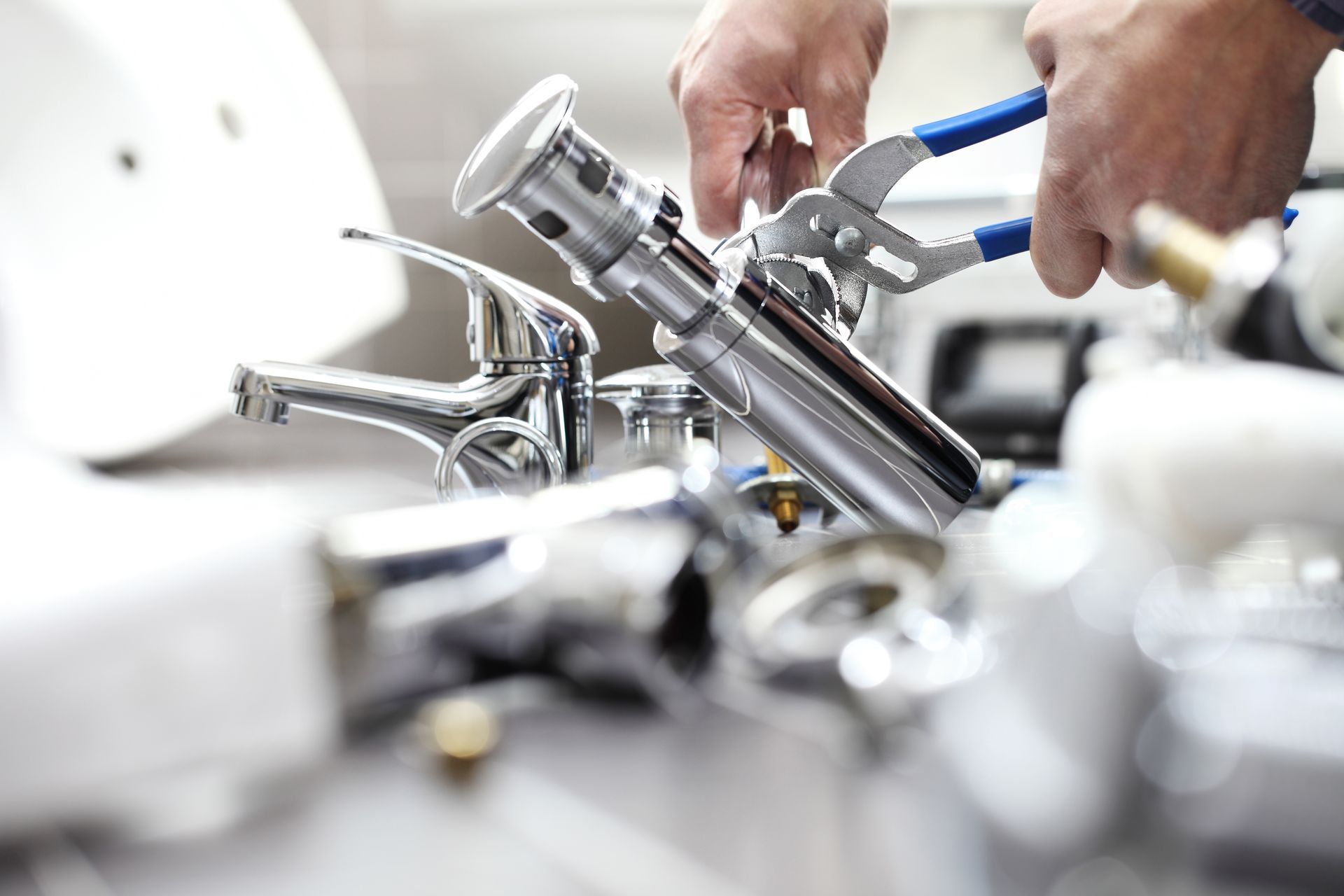 Close-up of hands using pliers to tighten a metal sink drain assembly on a workbench. Close-up of hands using pliers to tighten a metal sink drain assembly on a workbench.