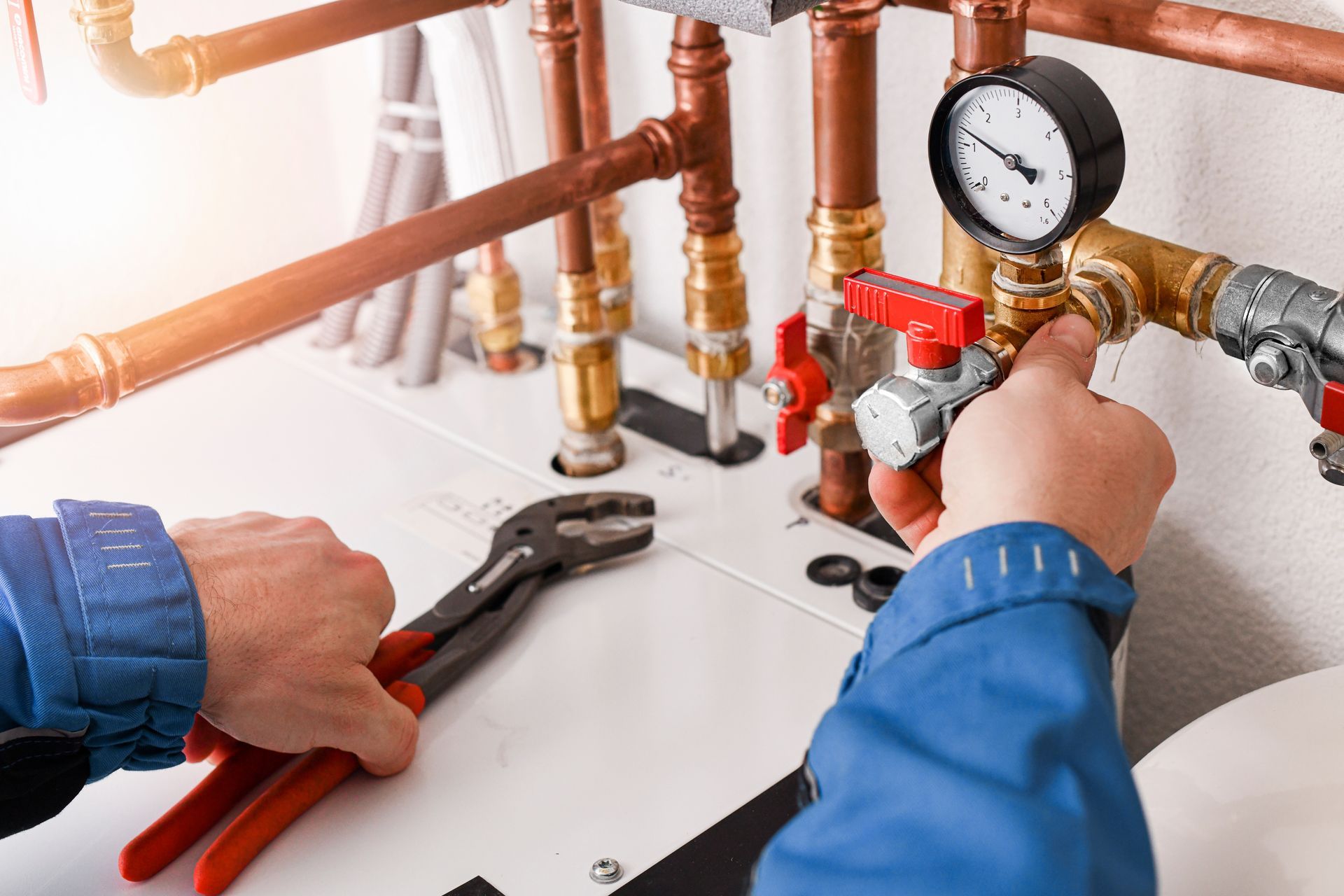 A technician in a blue uniform uses pliers and a valve on a copper-piped heating system.