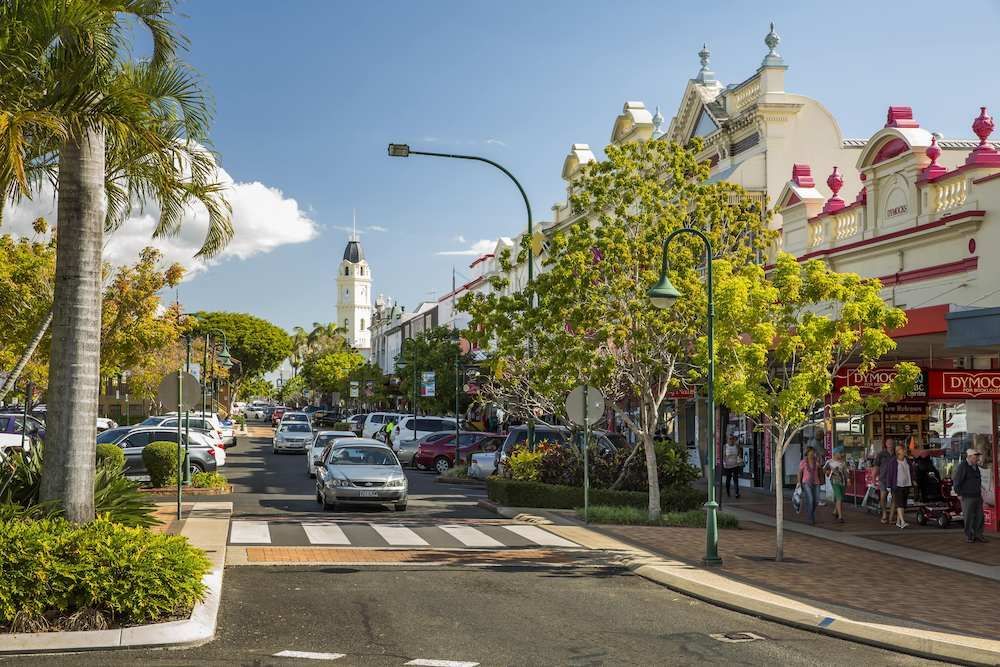 A Busy Street With Cars Driving Down It And A Clock Tower In The Background — ADK Coatings In Bundaberg, QLD