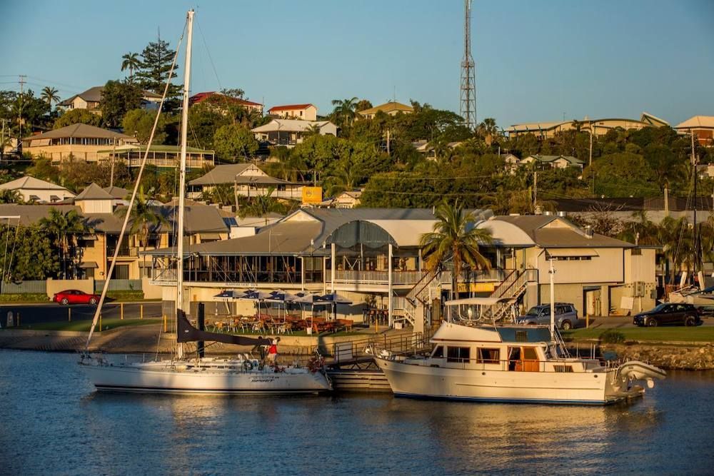 A Couple Of Boats Are Docked In A Harbor With Houses In The Background — ADK Coatings In Gladstone, QLD