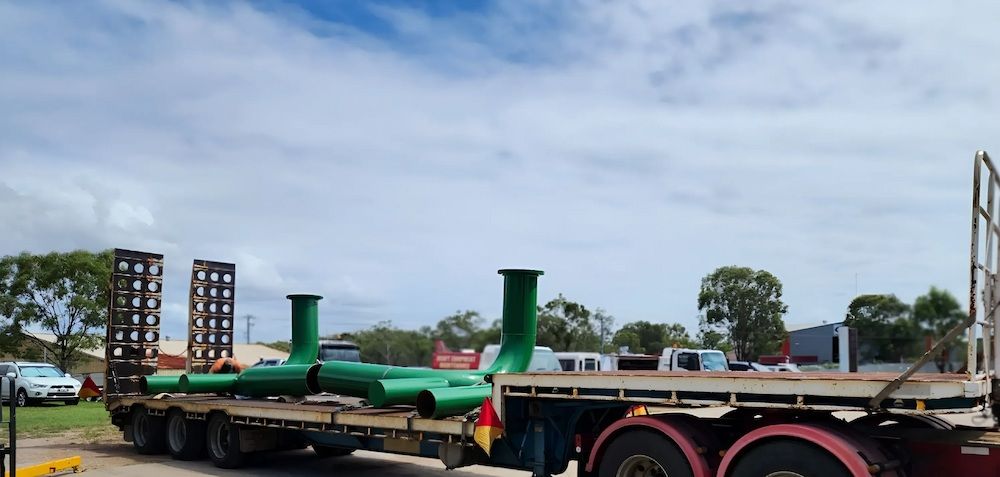 A truck is carrying green pipes on a flatbed trailer — ADK Coatings In Toolooa, QLD