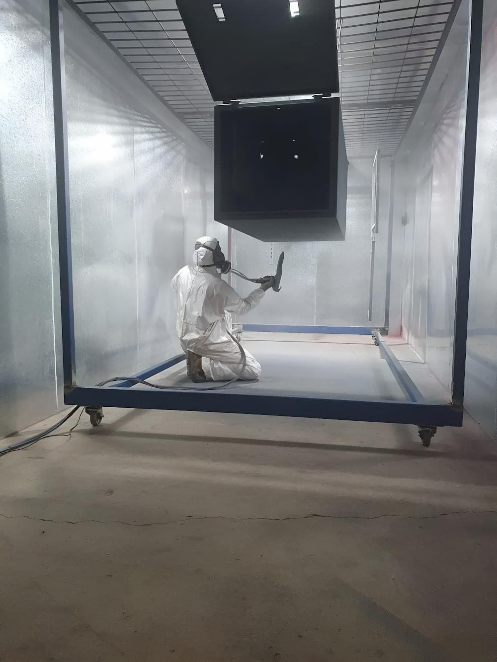 A Man Is Spray Painting A Piece Of Metal In A Room — ADK Coatings In Yeppoon, QLD