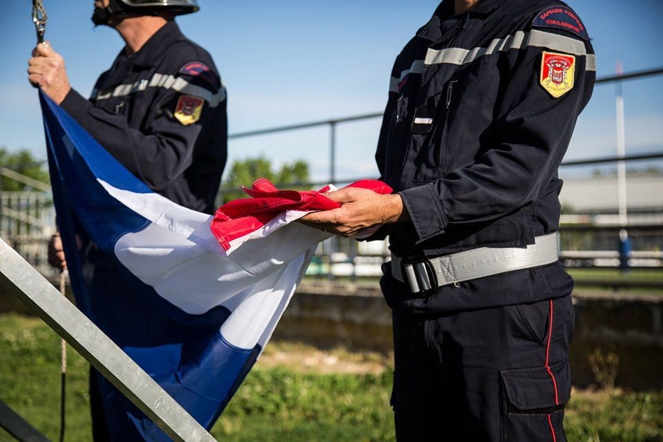Des sapeurs-pompiers de Marseille en uniforme en train de manipuler avec soin le drapeau français, symbolisant leur engagement et leur dévouement au service de la sécurité et de la protection des citoyens.