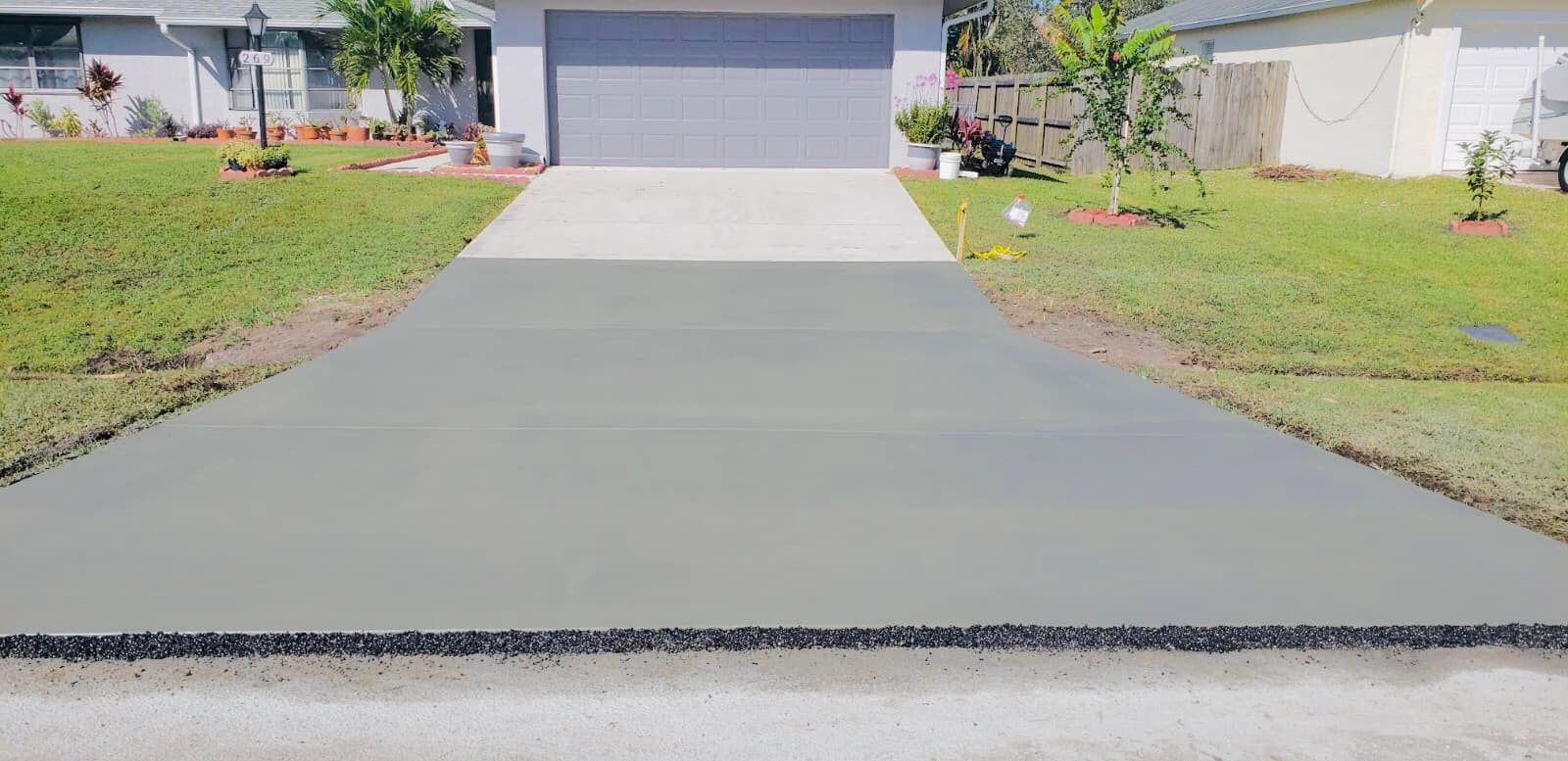 Freshly poured concrete driveway leading to a suburban house with a gray garage door, bordered by green grass.