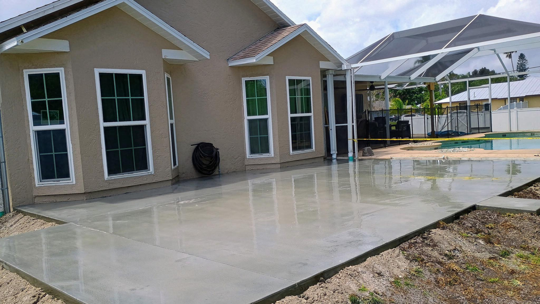Newly poured concrete patio next to a house with windows and an enclosed pool area.