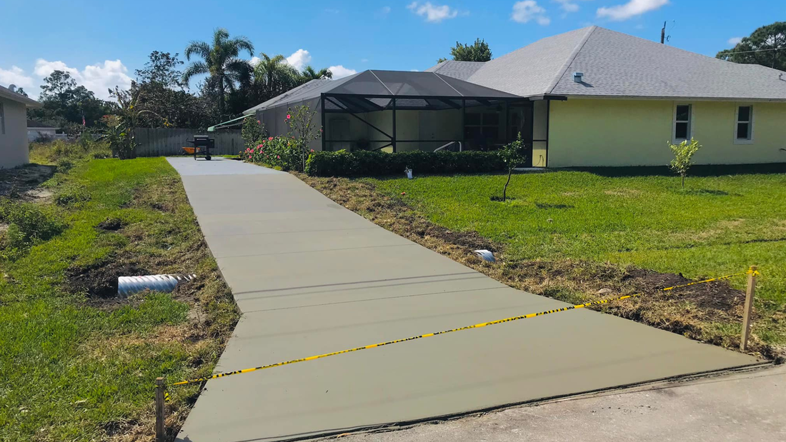 New concrete driveway leading to a yellow house with a screened porch, surrounded by grass.