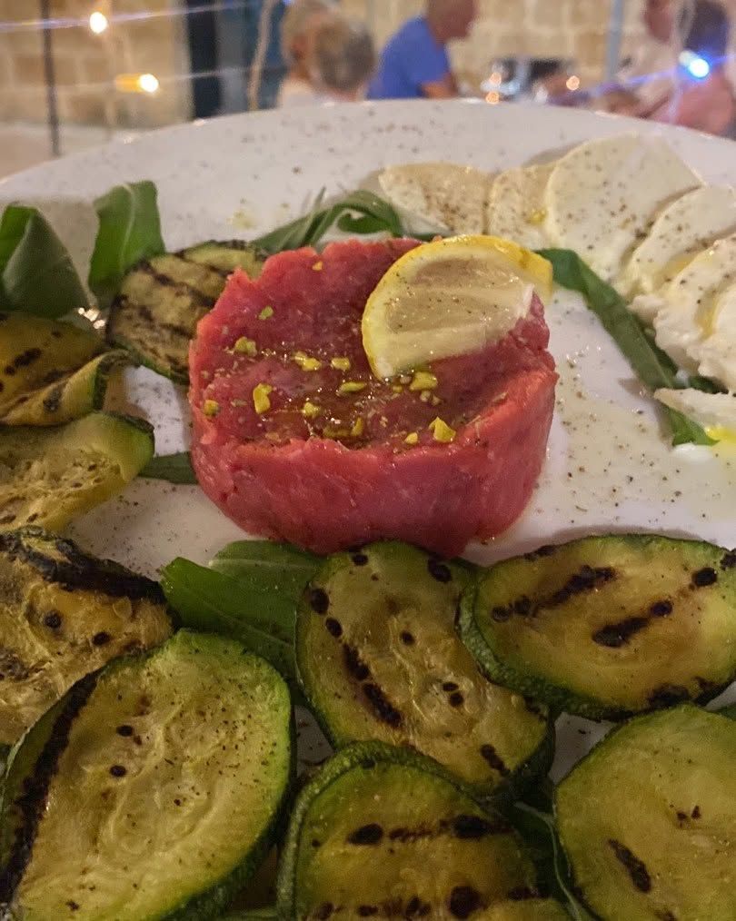 Tartare di tonno impiattato con limone, circondato da zucchine grigliate e guarnizione verde.