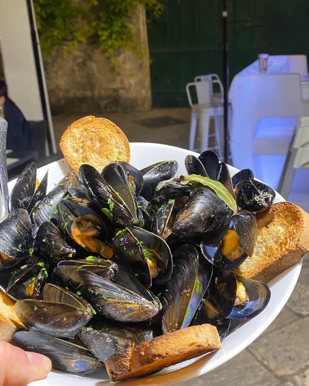 Piatto di cozze con gusci neri, accompagnato da pane tostato, servito all’aperto al tavolo di un ristorante