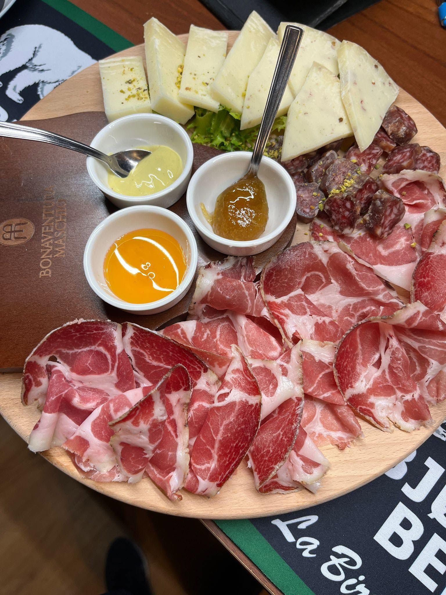 Tagliere di salumi con affettati, formaggi, miele e salse, servito su un vassoio di legno con le pinze