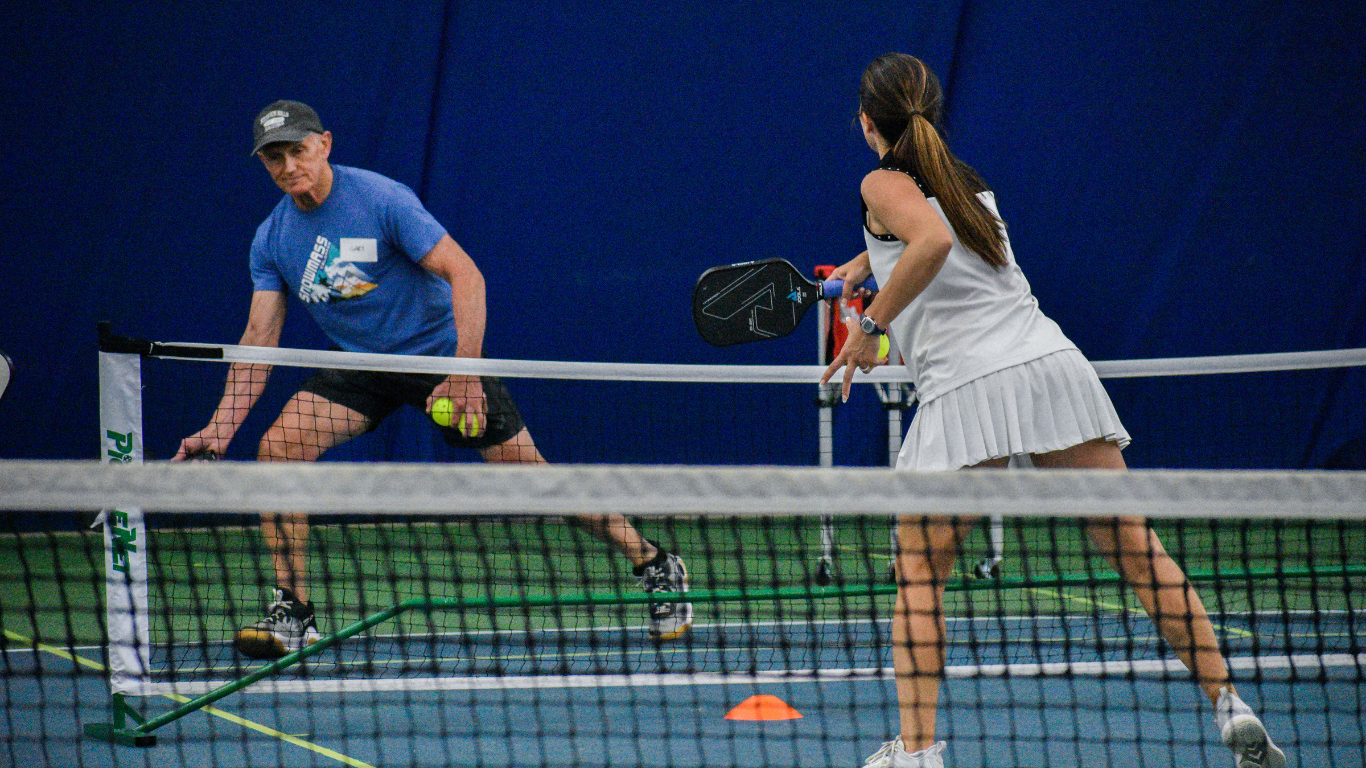 Two tennis players rally on a court, one in blue and one in white, near the net.