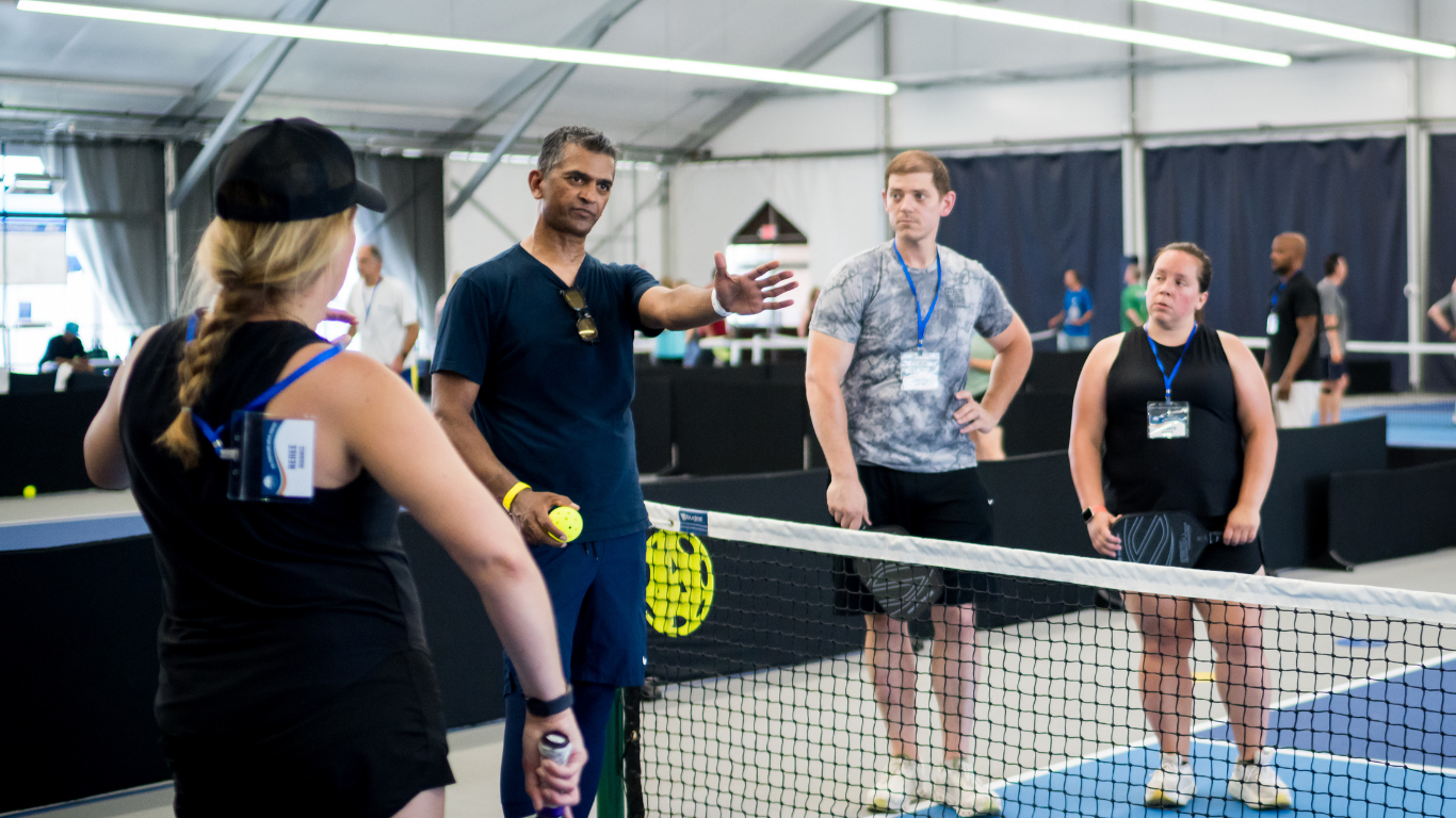 People standing around a ping-pong table in a bright indoor gym, discussing a game.