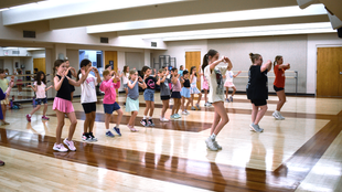 Group dance fitness class in a mirrored studio, with people exercising in colorful workout clothes.