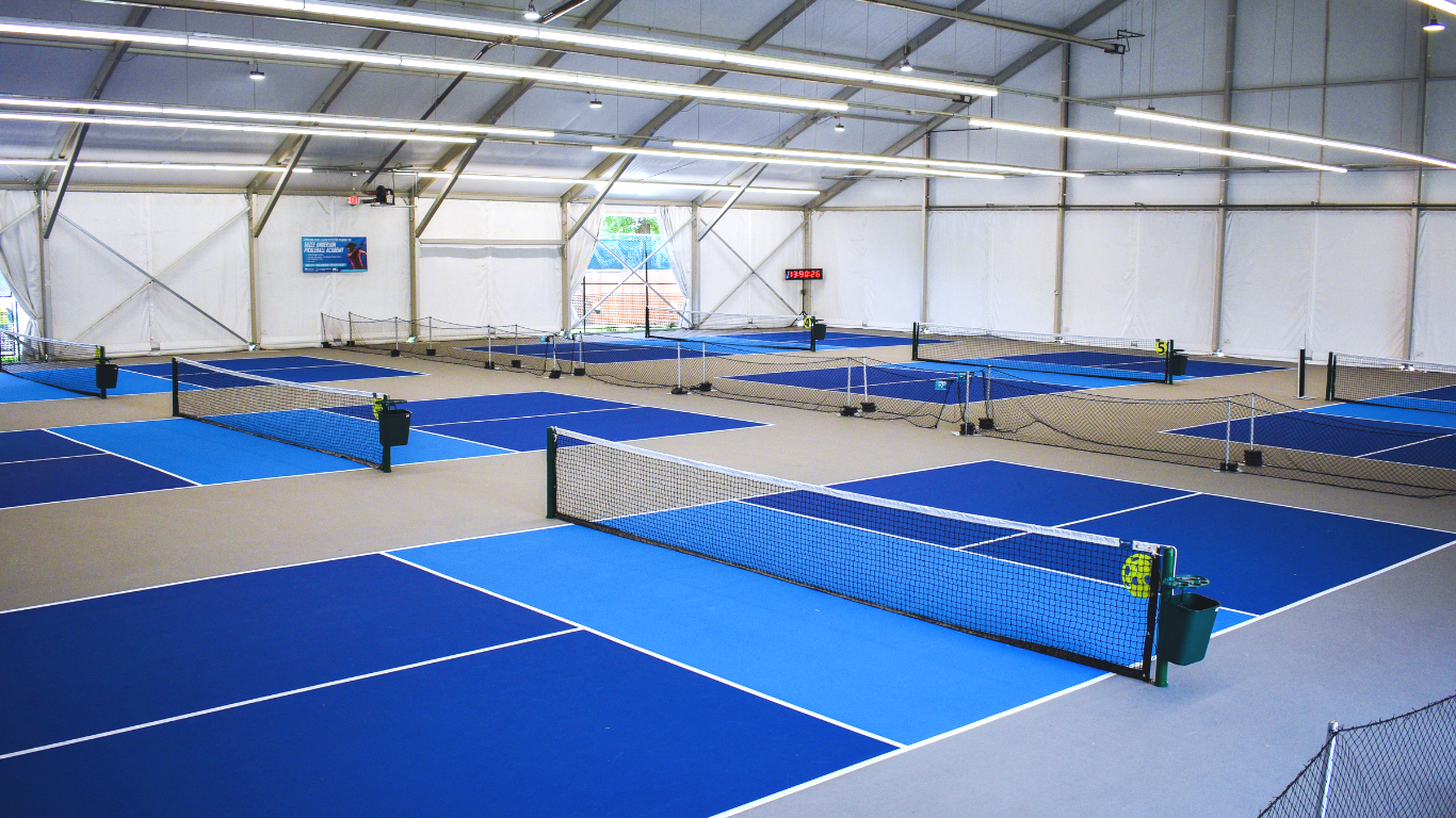 Indoor trampoline park with blue jumping surfaces and safety nets inside a large white tent.