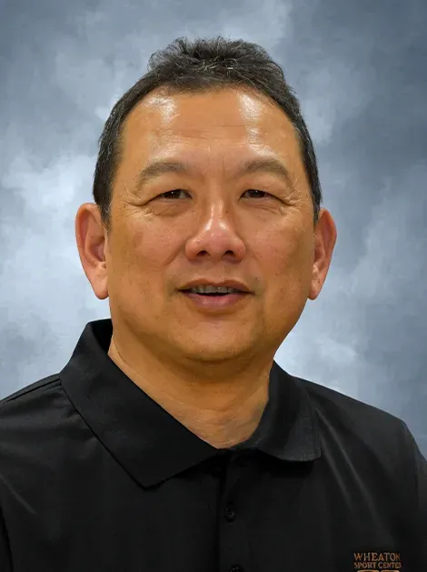 Portrait of a smiling man in a black polo shirt against a blue-gray studio backdrop