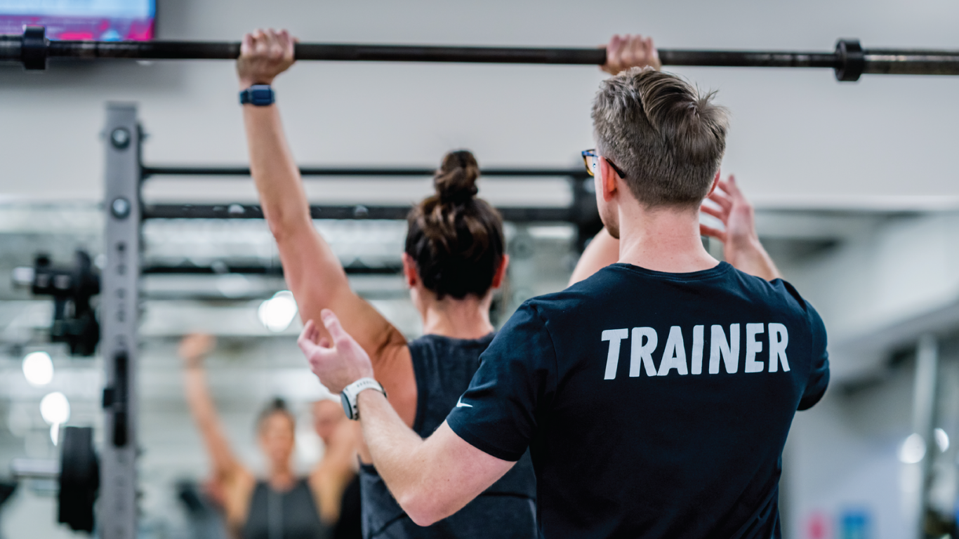Trainer coaching a person doing pull-ups in a gym