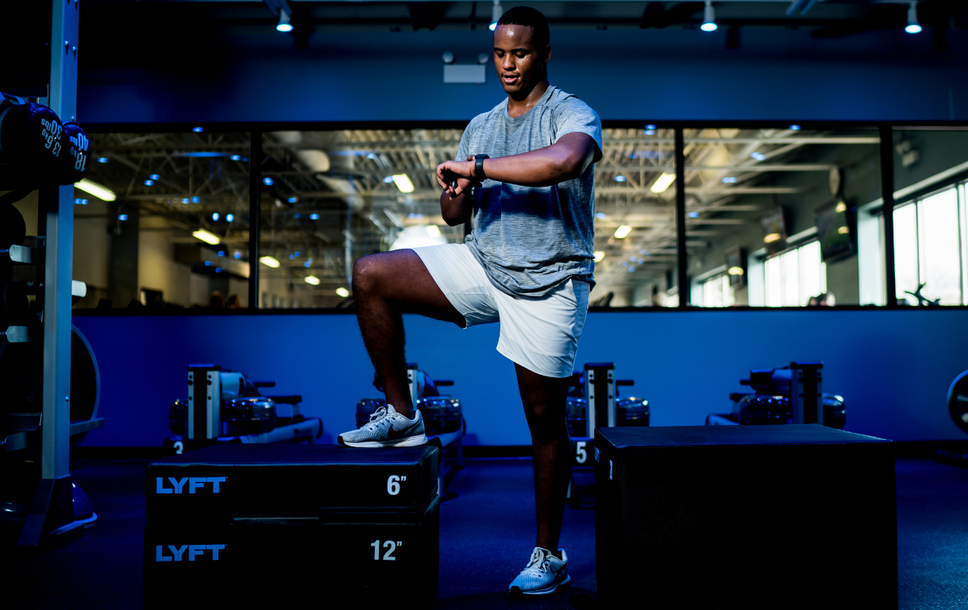 Person exercising on a plyometric box in a gym, balancing with one knee raised.