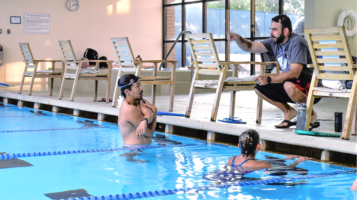 People in a pool taking part in an aquatic exercise session with a trainer on the deck.