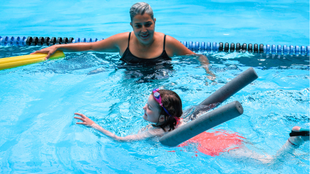 Adult and child in pool using a flotation noodle, smiling and playing in bright blue water
