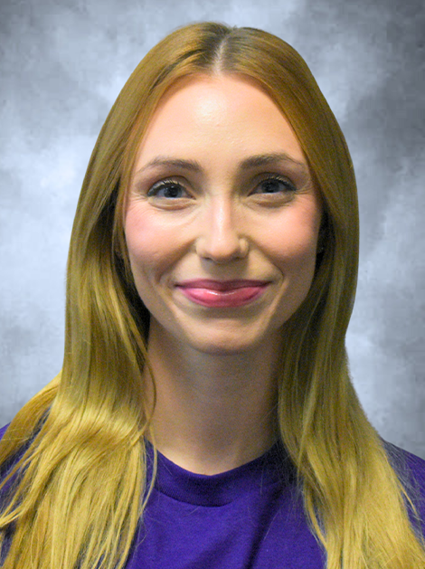 Portrait of a smiling person with long blonde hair wearing a purple top against a gray backdrop