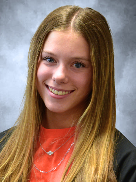 Smiling young woman with long blonde hair wearing an orange top and black jacket against a blue background