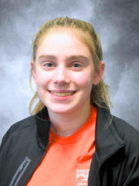 Smiling person in a black jacket over an orange shirt against a gray background