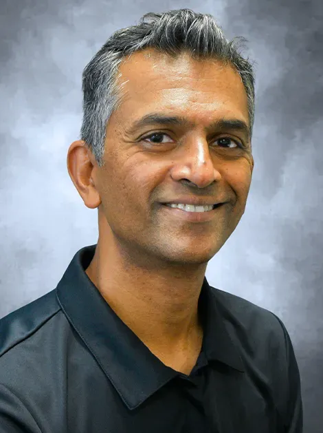 Smiling man in a dark polo shirt against a soft blue-gray studio background