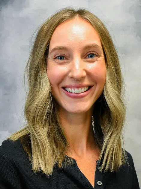 Smiling woman with shoulder-length blonde hair against a gray background